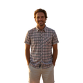Glas Apparel Hayes short sleeve shirt in a multi-colored plaid cotton pattern worn by a man on a beach at sunset.